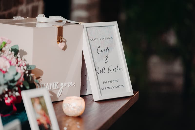 A wedding card box with a lock and a framed sign requesting guests to leave cards and well wishes for the new Mr & Mrs Searston, displayed on a wooden surface at Sandstone Point Hotel — Cellar.
