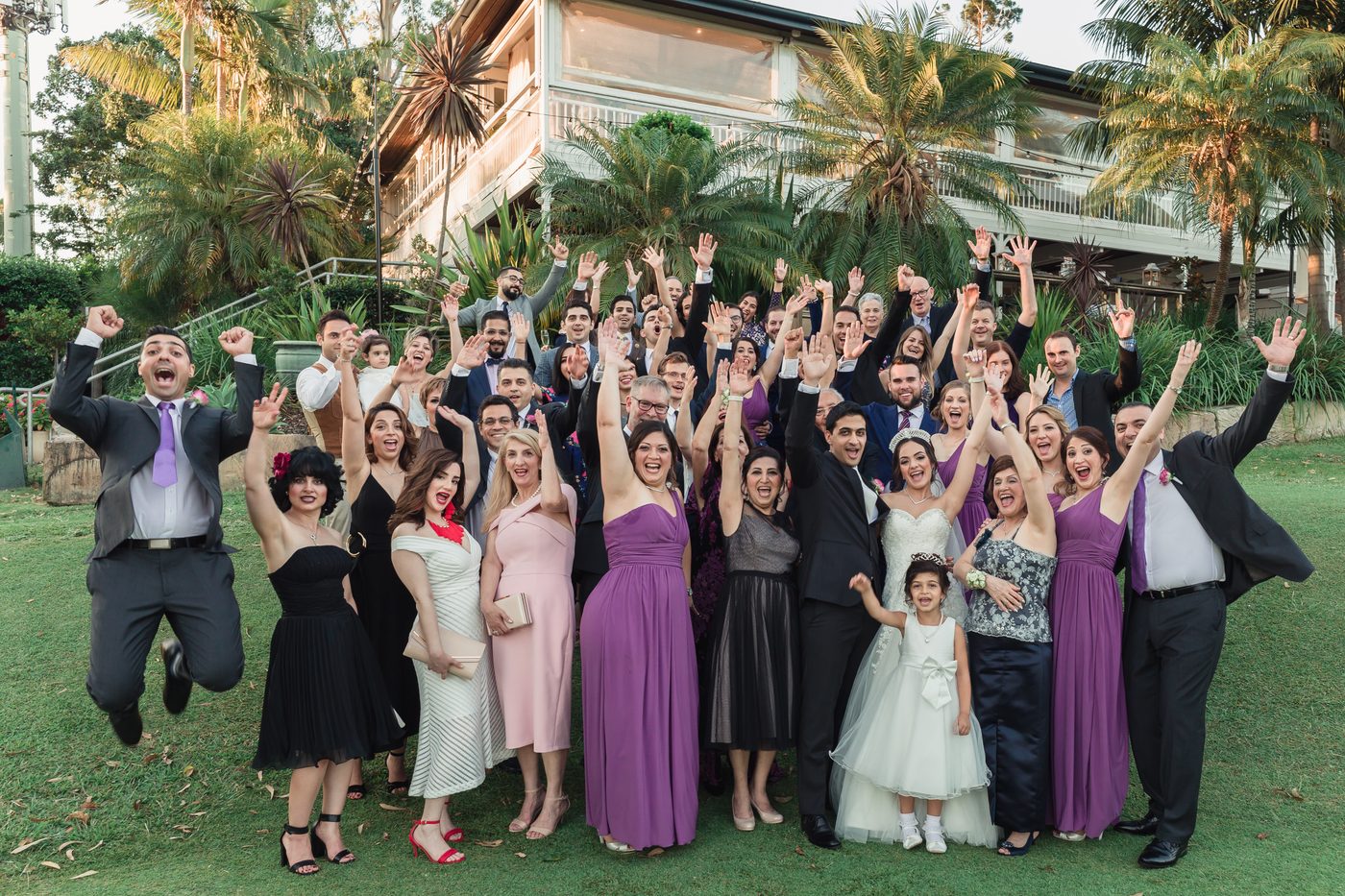 Pasha and Maryam pose with their wedding party and guests outside, all raising their hands and smiling. Destination wedding video packages by She Said Yes.