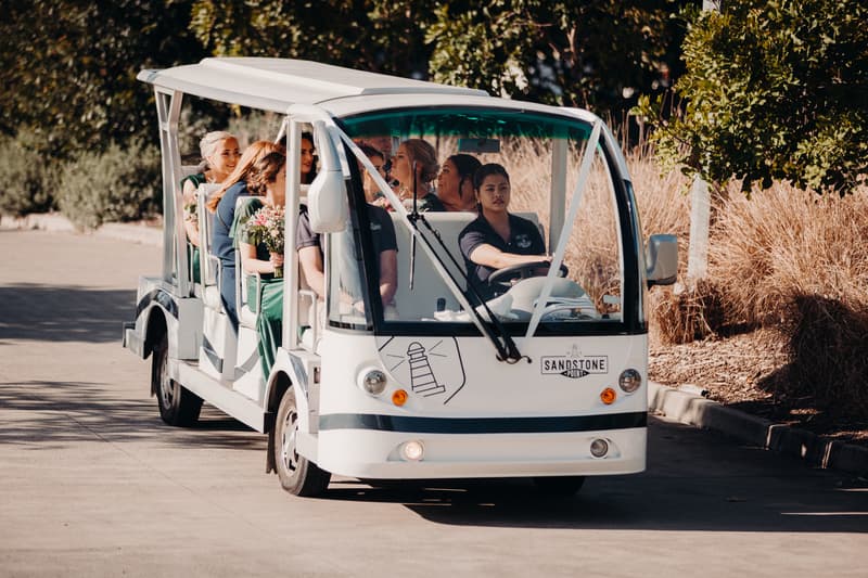 Bridesmaids seated in a white open-sided shuttle cart driven by a staff member at Sandstone Point Hotel — Pavilion.