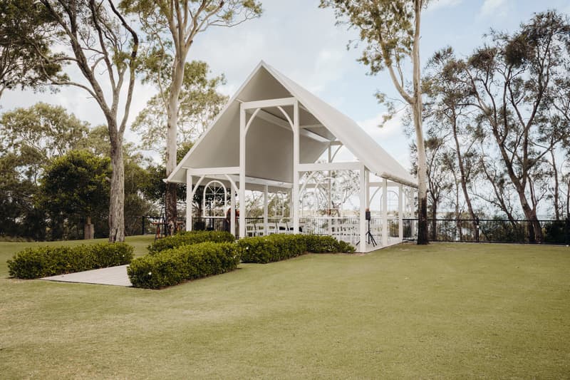 Empty white pavilion structure with chairs arranged inside, surrounded by green grass and trees at Sandstone Point Hotel — Pavilion.