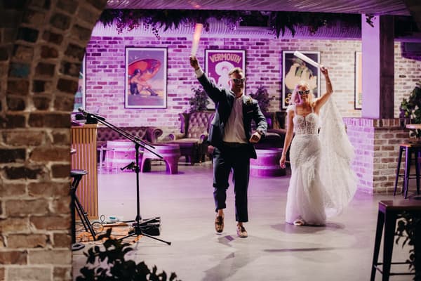 Bride Krystal and groom Brandon enter the reception stage at Sandstone Point Hotel — Cellar, each holding a light stick and wearing sunglasses.