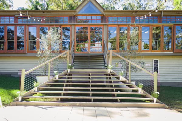 Empty wooden staircase decorated with small potted plants leading to a building with large glass windows at Kwila Lodge.