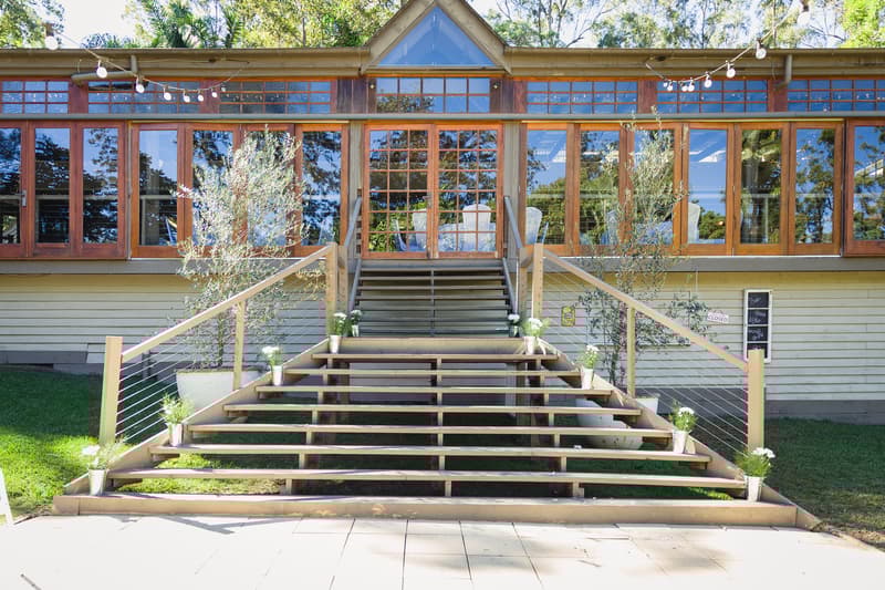 Empty wooden staircase decorated with small potted plants leading to a building with large glass windows at Kwila Lodge.
