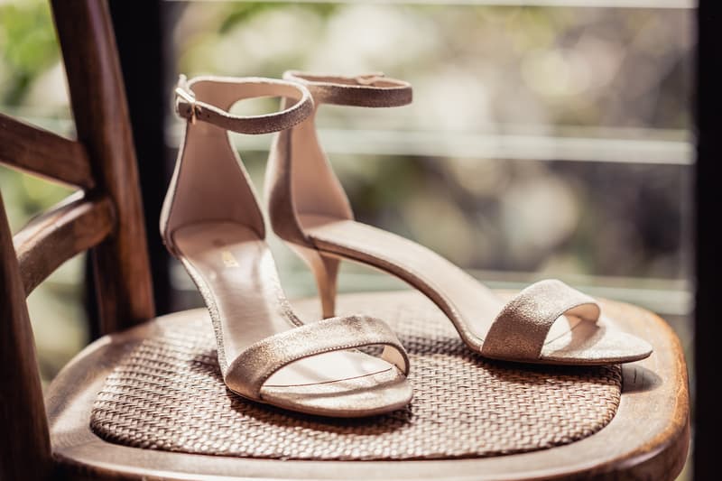A pair of beige high-heeled bridal shoes placed on a woven seat of a wooden chair at Toowong Rowing Club.