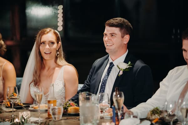 Chelsea the bride and Brent the groom sit at a table during the reception at Preston Peak Winery Functions Centre, with plates of food and drinks in front of them.