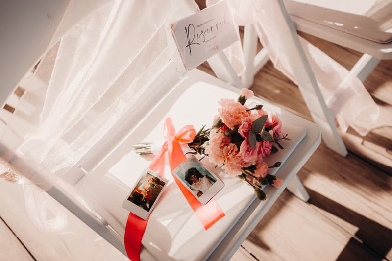 A white folding chair at Sandstone Point Hotel — Pavilion with a reserved sign, a bouquet of pink flowers tied with a coral ribbon, and two instant photos placed on the seat.