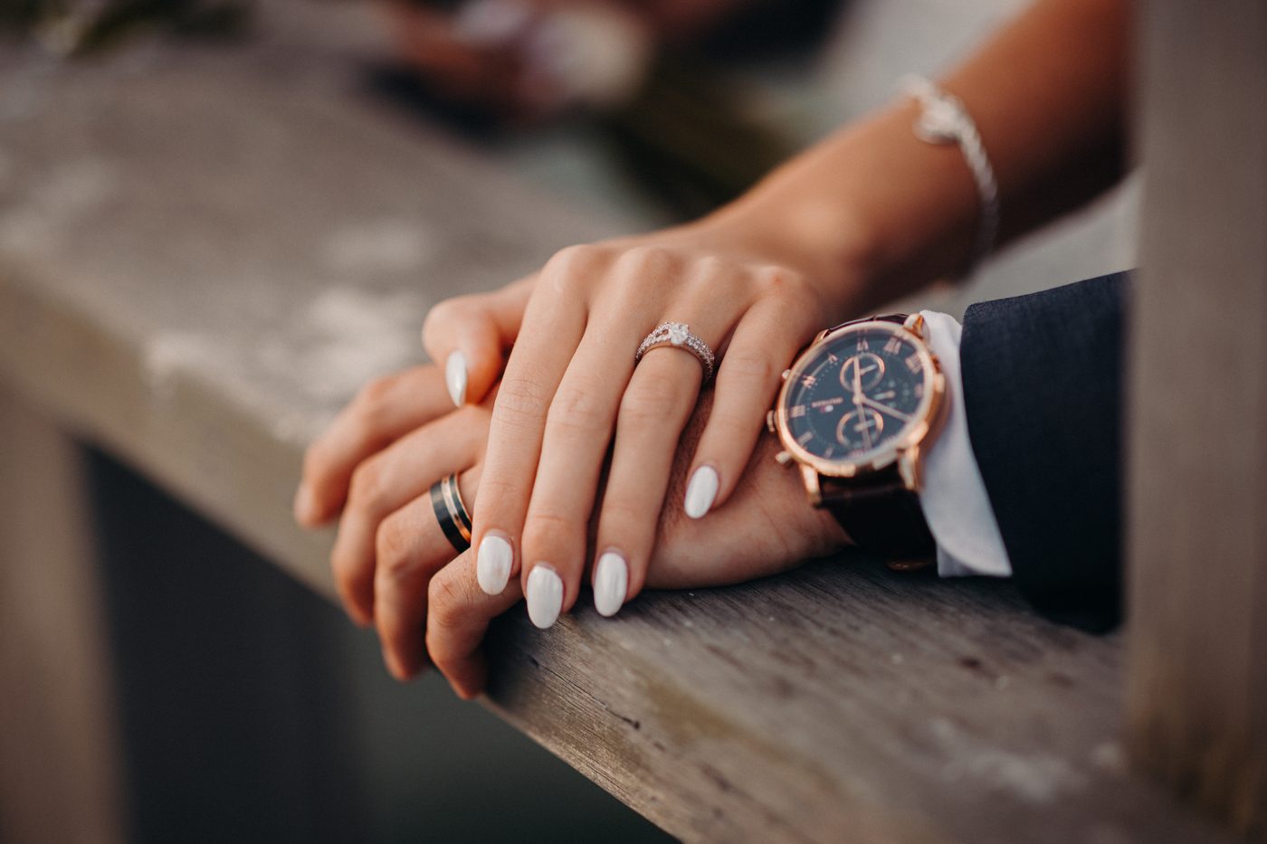Close-up of the bride's and groom's hands resting on a wooden surface, showing the bride's engagement ring and the groom's watch and wedding band. Engagement photography Brisbane by She Said Yes.