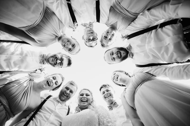 Annie the bride and Trent the groom stand in a circle with their bridal party at Ocean View Estates, all smiling and looking down toward the camera.