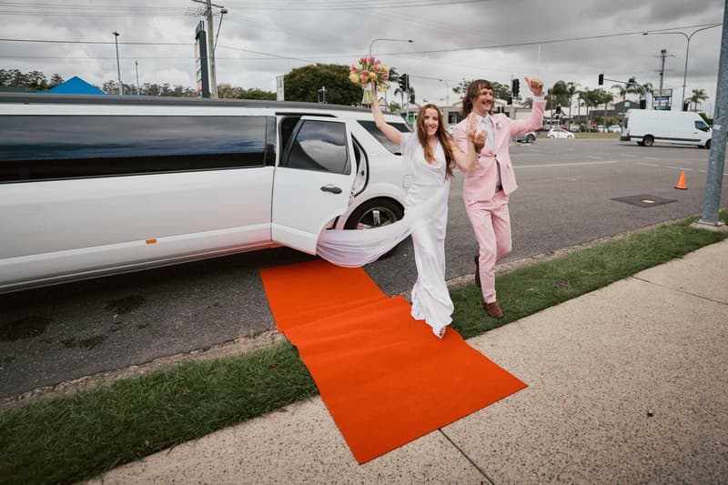 The bride Olivia and groom Jake step out of a white limousine onto a red carpet at White Horse Ranch, both raising their arms in celebration.