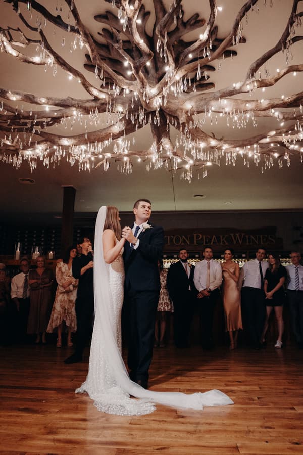 Chelsea and Brent share their first dance at the Preston Peak Winery Functions Centre with guests watching in the background under a large decorative chandelier.