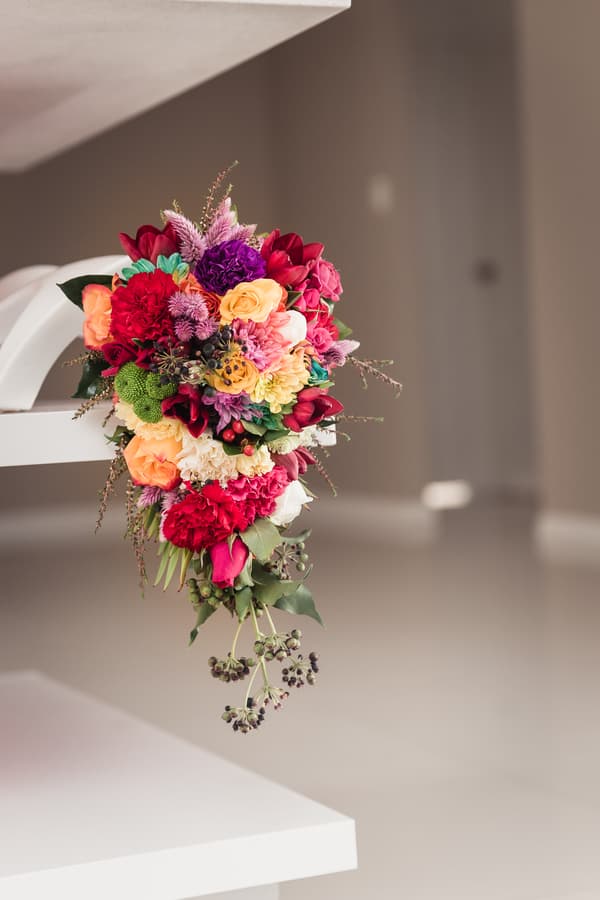 A colorful bridal bouquet with red, pink, orange, yellow, purple, and green flowers resting on a white surface at Kwila Lodge.