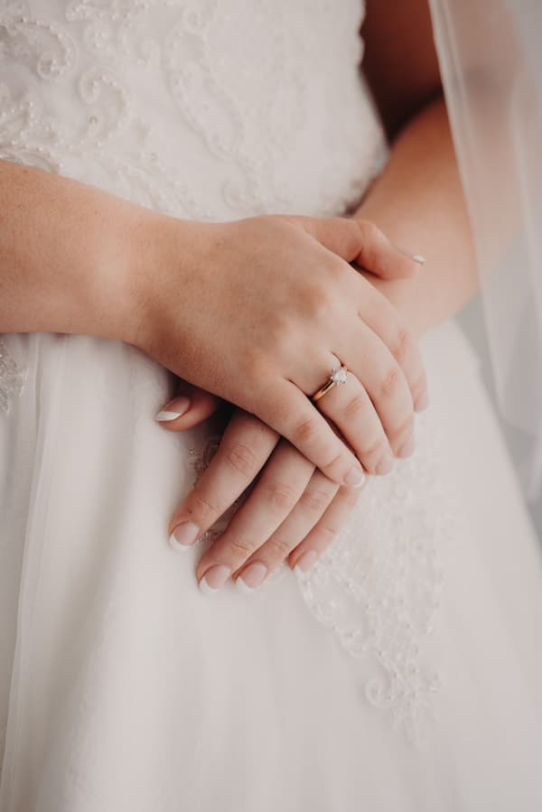 Close-up of the bride Emily's hands resting on her wedding dress at Sandstone Point Hotel.