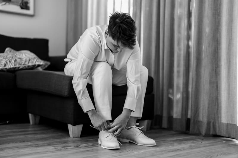 One bride sitting on a couch tying the laces of her white dress shoes indoors.