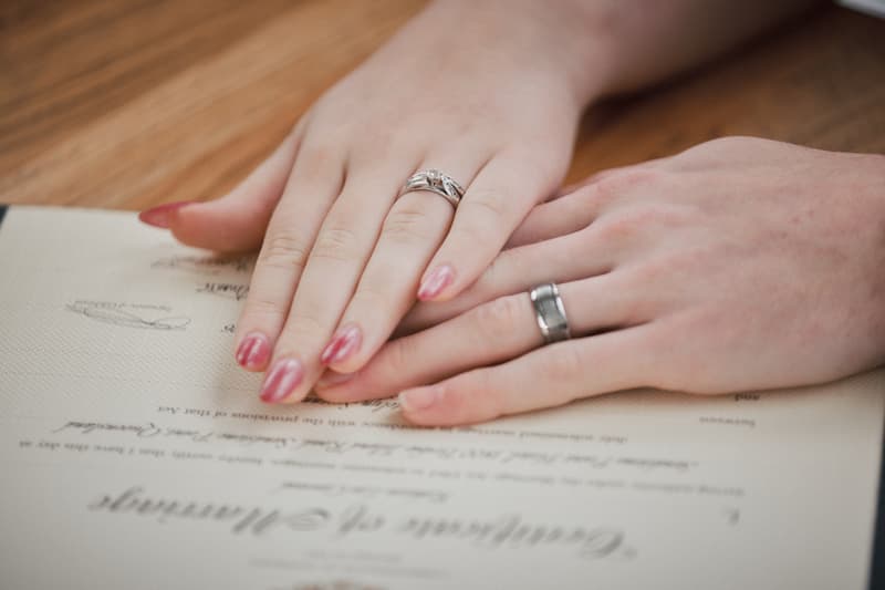 Close-up of the bride's and groom's hands resting on a marriage certificate at Sandstone Point Hotel — The Pavilion.