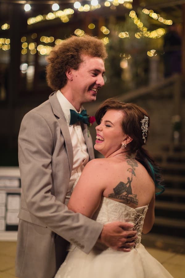 The bride Holly and groom Paul share a joyful moment dancing at the reception stage of Kwila Lodge, with fairy lights softly glowing in the background.