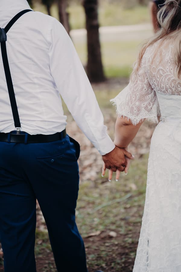 The bride Annie and groom Trent hold hands outdoors at Ocean View Estates, showing the back of their torsos and their joined hands.