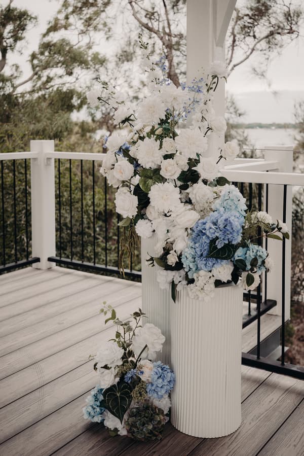 Floral arrangements with white and blue flowers displayed on white cylindrical stands on the pavilion deck at Sandstone Point Hotel.