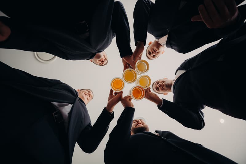 Five groomsmen in suits raise glasses of beer in a toast at Preston Peak Winery Functions Centre.
