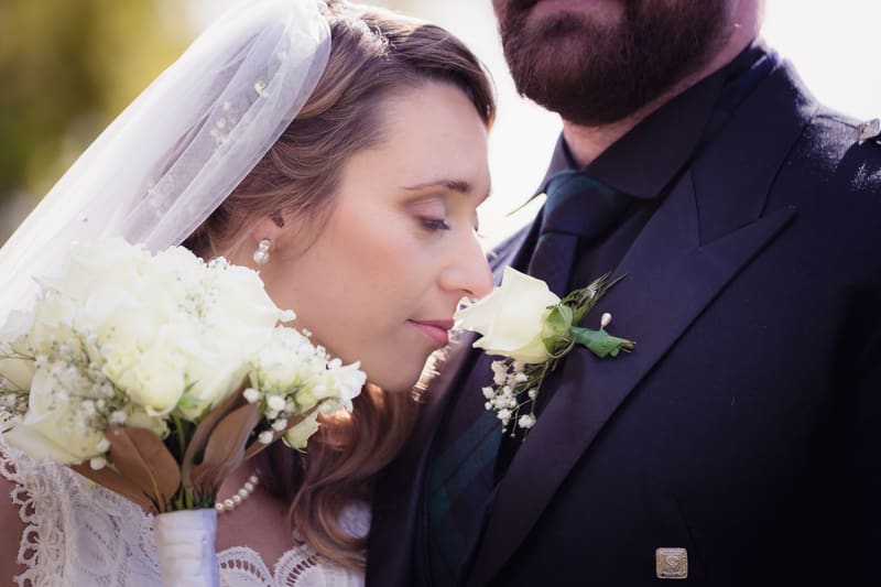 The bride Francesca leans close to the groom Ben's boutonniere while holding a bouquet of white flowers at the. Sunset wedding portraits Brisbane by She Said Yes.