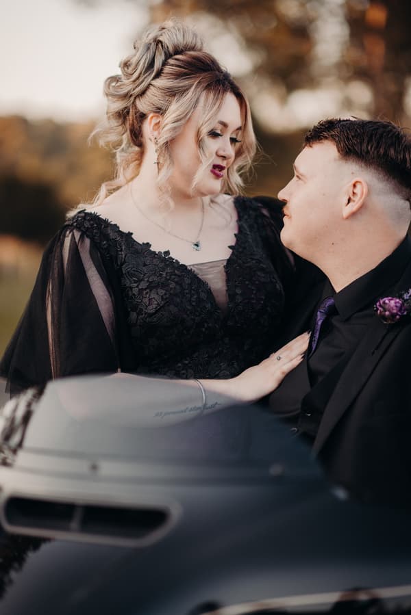 Renae the bride and Adam the groom pose together outdoors at Ocean View Estates, with Renae wearing a black lace dress and Adam in a black suit with a purple tie and boutonniere.