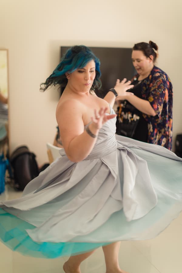 The bride with blue hair twirls in a strapless grey dress while another woman stands in the background inside a room at Kwila Lodge.