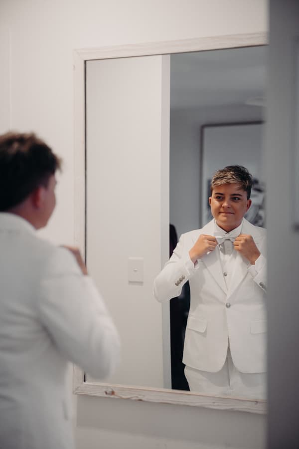 Tiffany adjusts her bow tie while looking at herself in a mirror during bridal preparation.