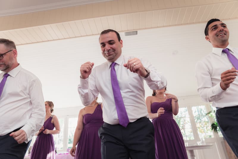 Groomsmen and bridesmaids dancing indoors at Hillstone St Lucia — The Quartyard, with men wearing white shirts and purple ties and women in purple dresses.
