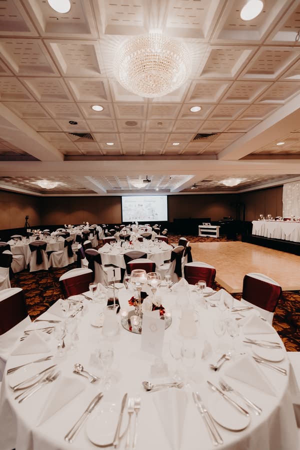 Reception hall at Royal on the Park set with round tables covered in white tablecloths, neatly arranged silverware, glassware, and centerpieces, with a dance floor and head table visible in the background.