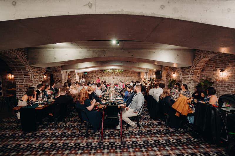 Guests seated at long banquet tables inside the Cellar at Sandstone Point Hotel during the wedding reception.