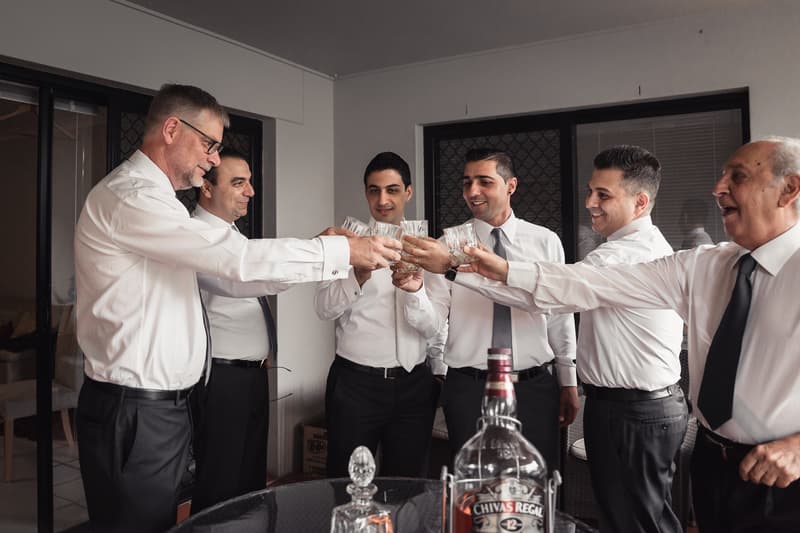 Six men in white shirts and ties raise glasses in a toast indoors at Hillstone St Lucia — The Quartyard.