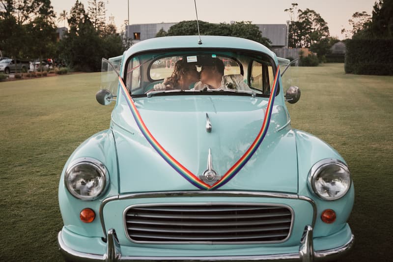 Mandy and Selina share a kiss inside a vintage light blue car decorated with rainbow ribbons at Sandstone Point Hotel grounds.