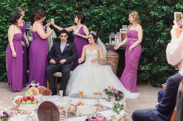 Bride Maryam and groom Pasha seated outdoors surrounded by bridesmaids in purple dresses at Hillstone St Lucia — The Quartyard, with a low table set with food and flowers in front of them.