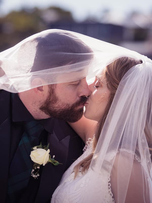 Francesca and Ben share a kiss with Francesca's veil draped over both of them at Toowong Rowing Club — The Malouf Room, with water and blurred greenery in the background.