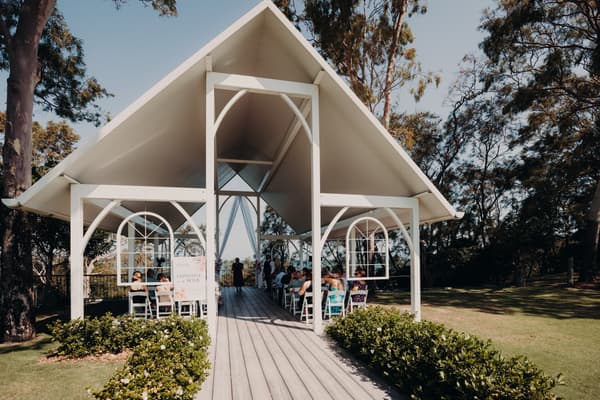 Guests seated under the pavilion at Sandstone Point Hotel for the wedding ceremony of Chantelle and Peter, with the officiant standing at the altar.