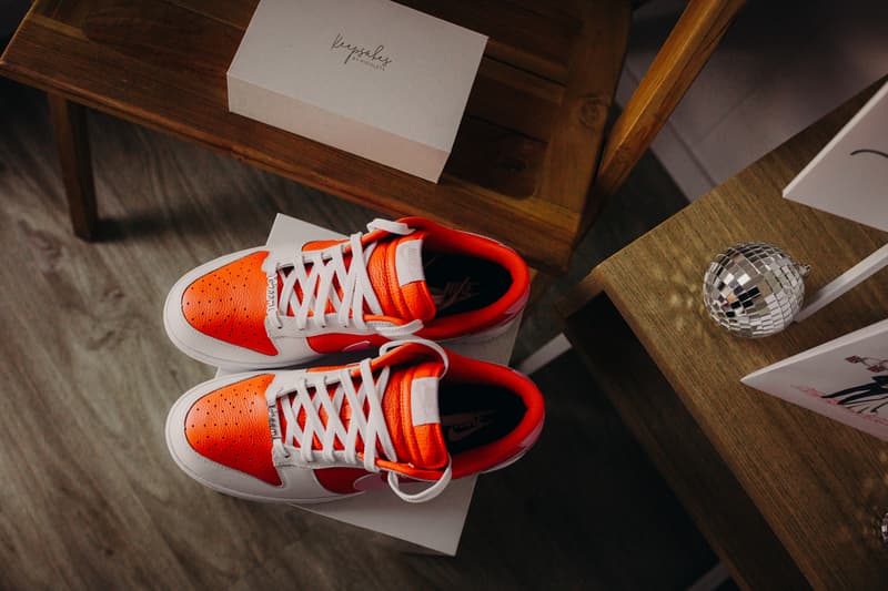 A pair of orange and white Nike sneakers placed on a white box on the floor next to wooden furniture, with a small disco ball and wedding cards on a nearby table at Sandstone Point Hotel.