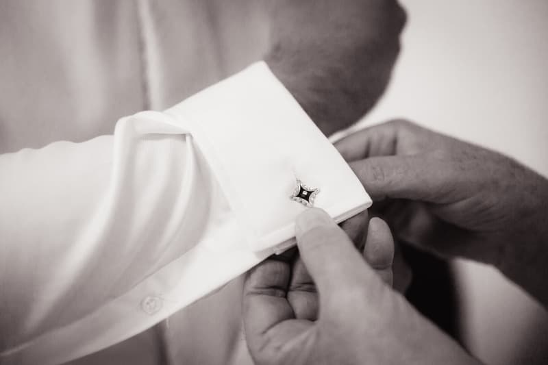 Close-up of hands fastening a cufflink on a groom's white dress shirt sleeve.