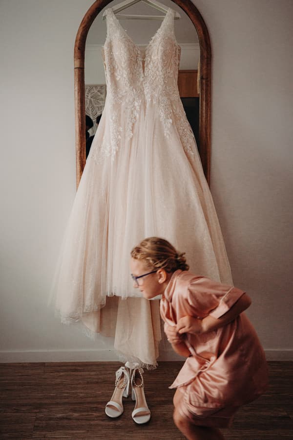 The bride's wedding dress hangs on a mirror at Sandstone Point Hotel, with a young girl in a pink satin robe crouching nearby.