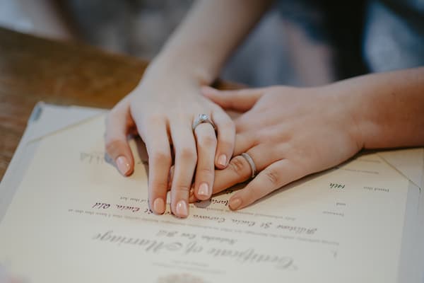 Close-up of two hands wearing wedding rings resting on a marriage certificate.