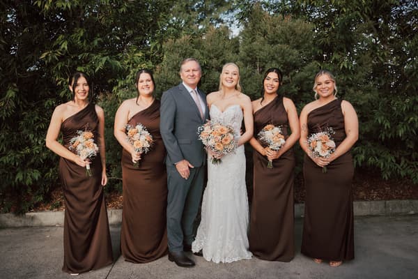 The bride Morgan stands with four bridesmaids in matching brown dresses and a man in a suit, likely the bride's father, posing outdoors. Lead follow-up communication delay by She Said Yes.