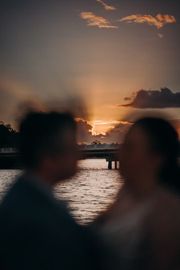 Silhouetted bride and groom facing each other near water at sunset with a bridge in the background at Sandstone Point Hotel.