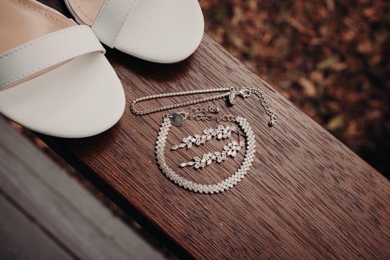 Close-up of white bridal shoes and silver jewelry including a bracelet and earrings placed on a wooden surface at Sandstone Point Hotel.