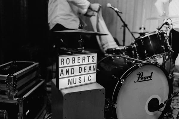 A drum set with a Pearl bass drum and a lightbox sign reading 'ROBERTS AND DEAN MUSIC' at Yabbaloumba Retreat — The Shed.