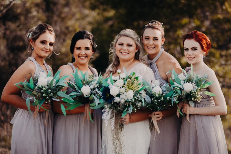 The bride Annie stands with four bridesmaids outdoors at Ocean View Estates, all holding bouquets and smiling at the camera.