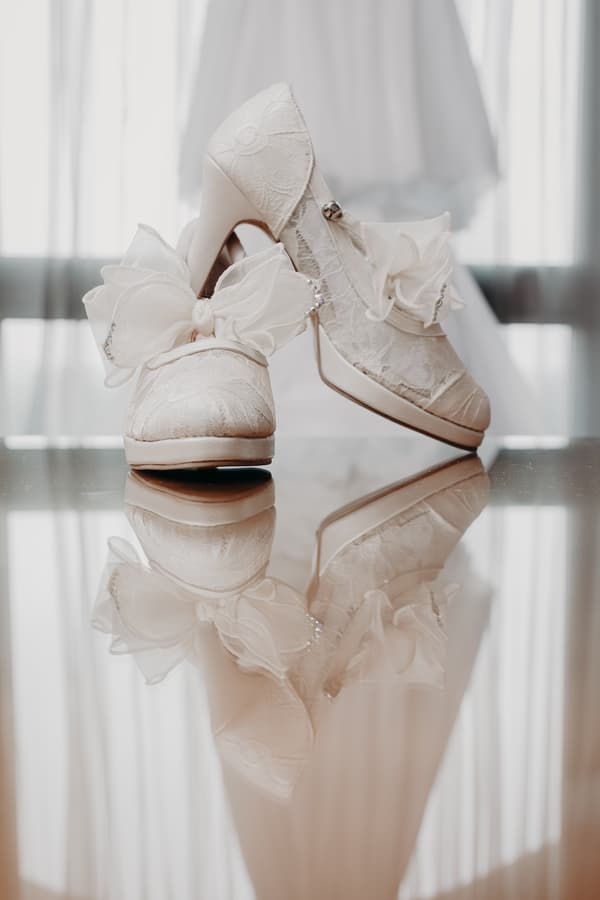 Close-up of the bride's white lace wedding shoes with large decorative bows, reflected on a polished surface at Royal on the Park.