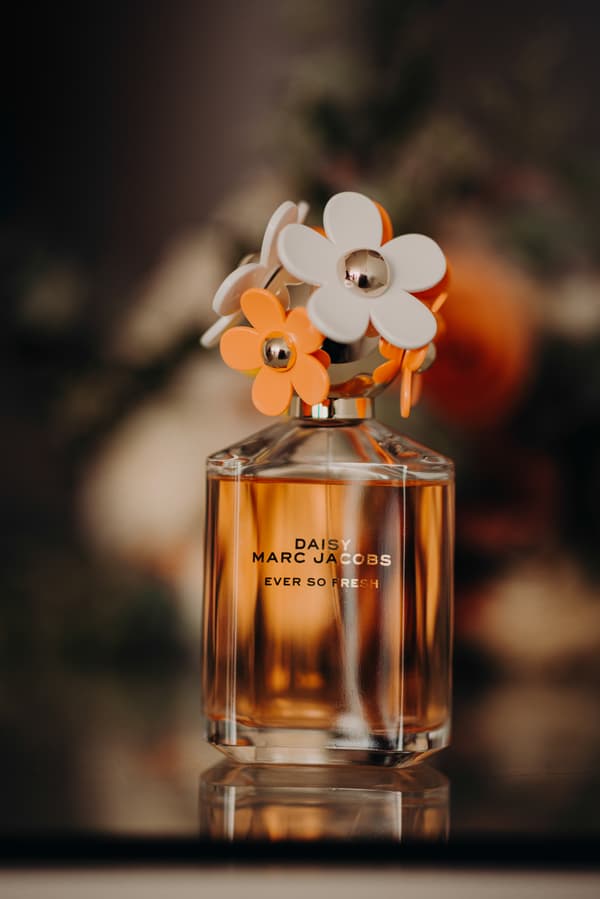 Close-up of a Daisy Marc Jacobs Ever So Fresh perfume bottle with decorative white and orange flower caps.
