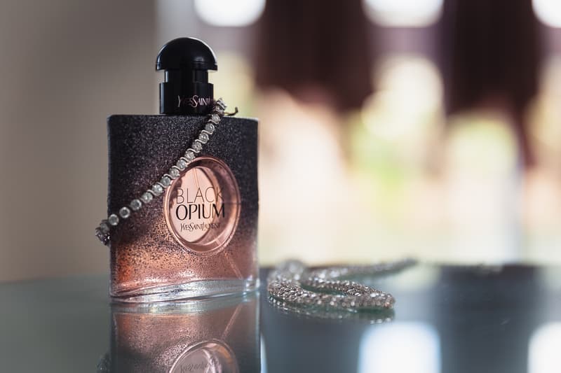 Close-up of a Yves Saint Laurent Black Opium perfume bottle with a silver necklace draped over it, placed on a reflective surface at Novotel Sunshine Coast Resort.