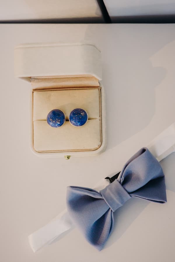 A pair of blue cufflinks in a beige box and a blue bow tie on a white surface.
