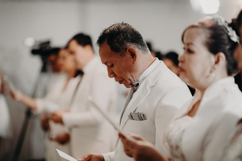 Guests dressed in white stand in a row holding papers during the ceremony at Royal on the Park.
