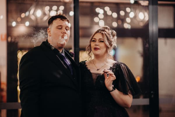 The bride Renae and groom Adam stand together inside the Ocean View Estates Function Room during the reception stage, both holding cigars with smoke visible around Adam.