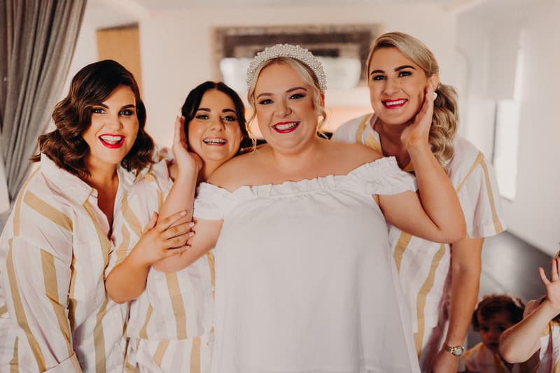 The bride Jacquelyne poses indoors with three bridesmaids wearing matching striped shirts at Sandstone Point Hotel.